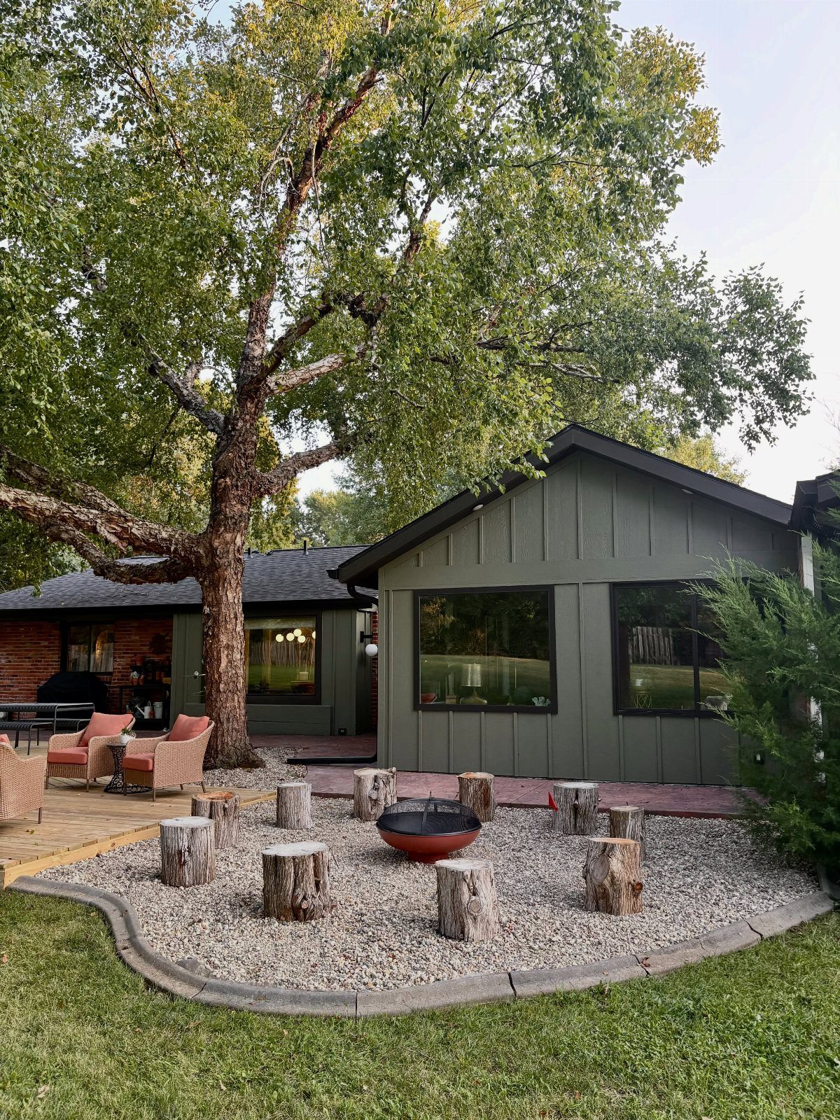 10 Around a Tree Ideas for Better Outdoor Spots 10 A large tree provides shade over a backyard fire pit area with wooden stump seating.