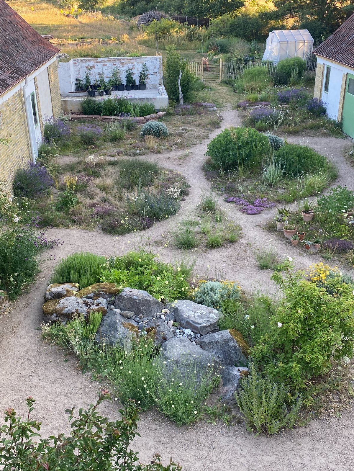 18 Big Backyard Garden Ideas for Every Budget 18 Winding gravel pathways through a lush garden filled with green shrubs and purple flowers.