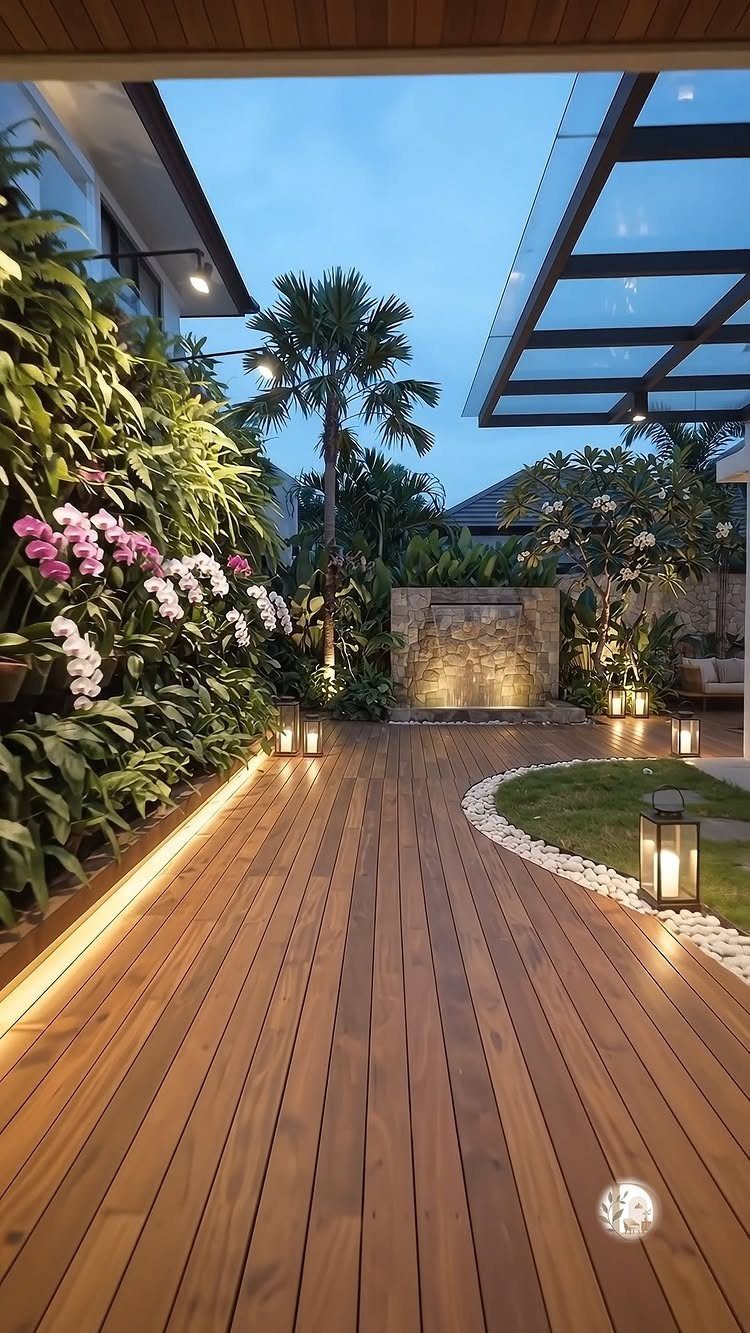 18 Big Backyard Garden Ideas for Every Budget 7 Wooden deck in a lush garden with a vertical orchid wall and stone water feature at dusk.