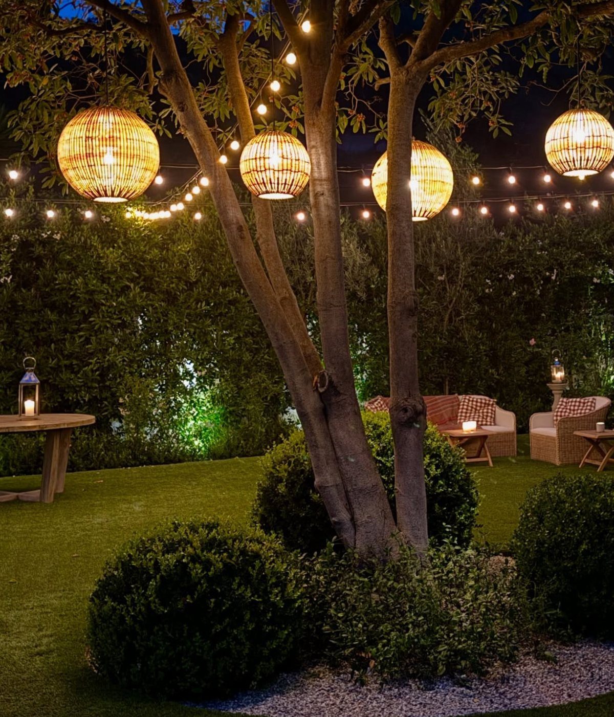 18 Big Backyard Garden Ideas for Every Budget 9 Woven spherical lanterns and string lights hanging from trees in a lush backyard garden at night.