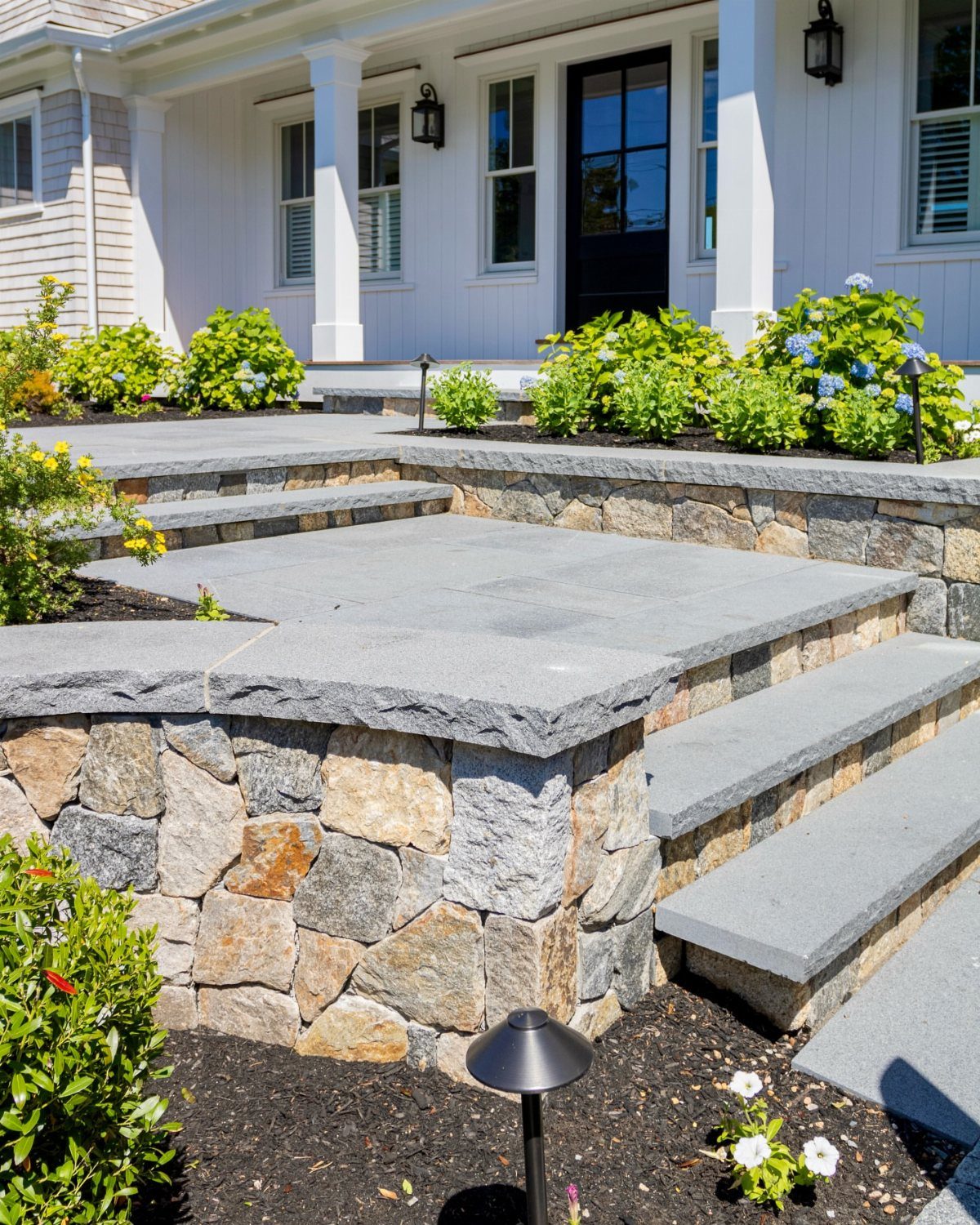 10 Cape Cod Front Yard Landscaping Ideas for Classic Charm 5 Stone steps with grey flagstone treads and natural stone retaining walls leading to a white house.