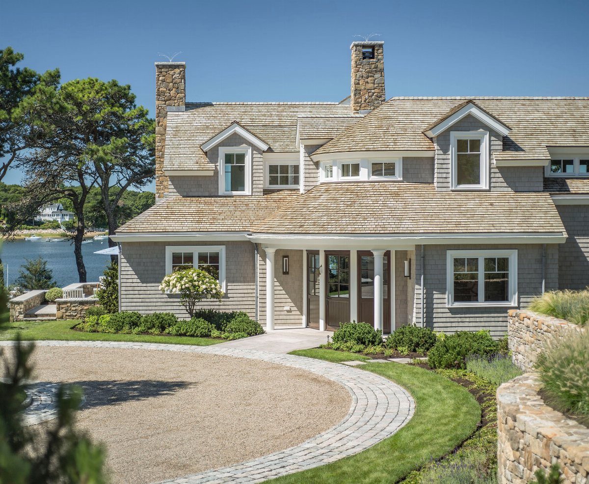 10 Cape Cod Front Yard Landscaping Ideas for Classic Charm 7 A Cape Cod style house featuring manicured landscaping, stone walls, and a gravel driveway with pavers.