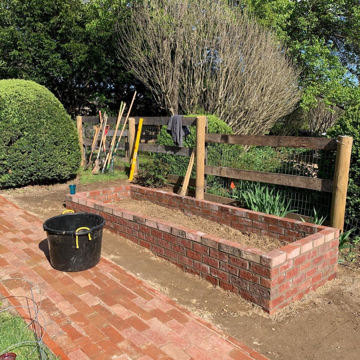 Cheap Raised Garden Beds for 4 DIY Builds 1 Red brick raised garden bed situated next to a brick walkway in a garden.