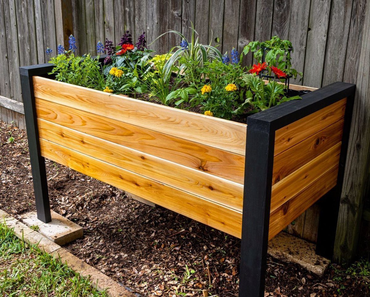 Cheap Raised Garden Beds for 4 DIY Builds 3 A wooden raised garden bed with black corner posts filled with colorful blooming flowers.