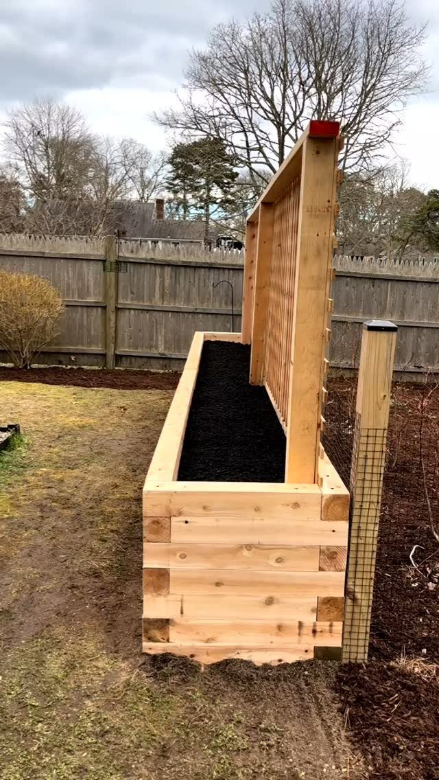 Cheap Raised Garden Beds for 4 DIY Builds 4 A long wooden raised garden bed filled with dark soil next to a wooden fence.