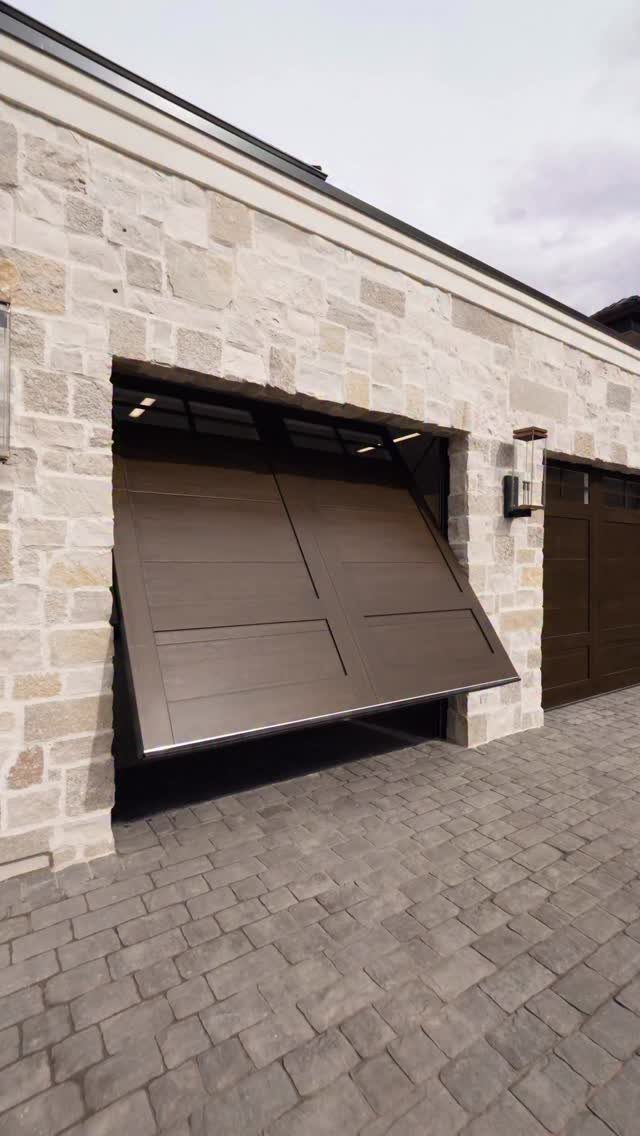 Craftsman Style Garage Doors: 8 Ideas from Carriage House to Modern Grey 8 A dark brown wooden garage door opening outward from a light stone building onto a cobblestone driveway.