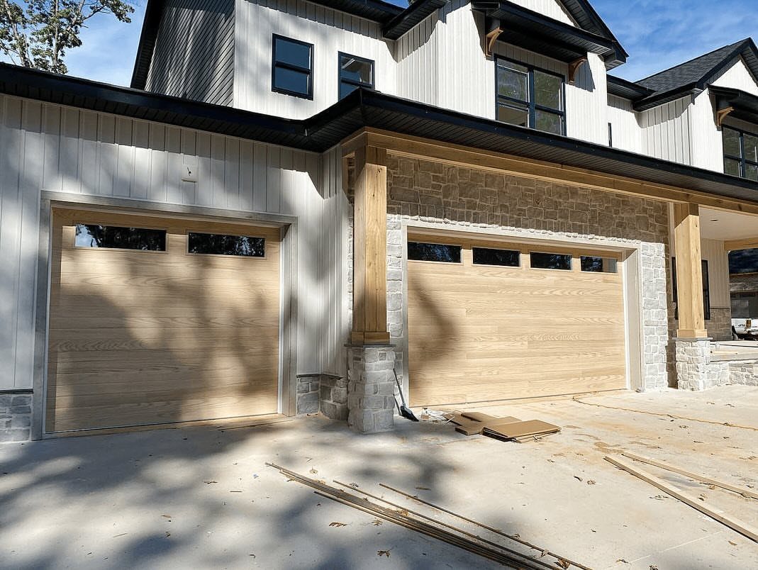 Craftsman Style Garage Doors: 8 Ideas from Carriage House to Modern Grey 4 Two light wood garage doors with small windows on a white and stone house.