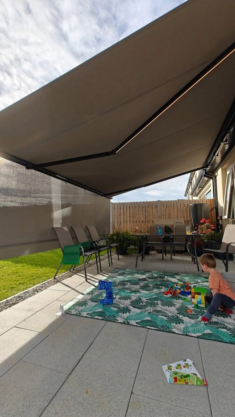 17 Deck Covering Ideas for Shade, Style & Rain Shelter 3 A large grey retractable awning provides shade over a patio where a child plays with blocks.