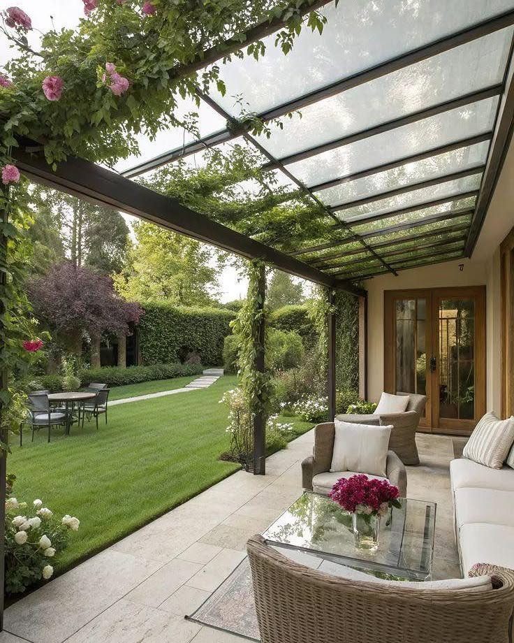 17 Deck Covering Ideas for Shade, Style & Rain Shelter 14 A glass roof pergola with climbing roses covering a stone patio and outdoor lounge area.