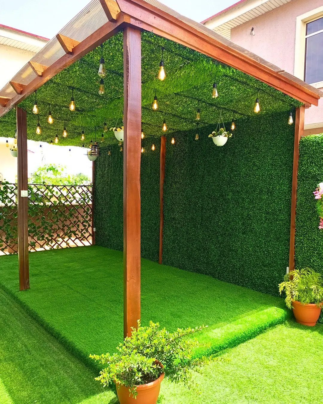 17 Deck Covering Ideas for Shade, Style & Rain Shelter 13 Wooden pergola structure with green foliage walls and ceiling, decorated with hanging string lights.