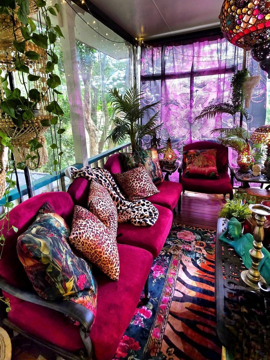 17 Deck Covering Ideas for Shade, Style & Rain Shelter 8 Red velvet sofas with leopard print pillows sit under purple sheer curtains in a lush outdoor space.