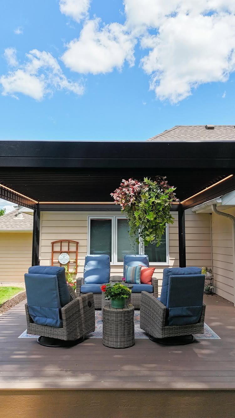 17 Deck Covering Ideas for Shade, Style & Rain Shelter 1 Black louvered pergola covering a wooden deck with blue wicker patio furniture and plants.
