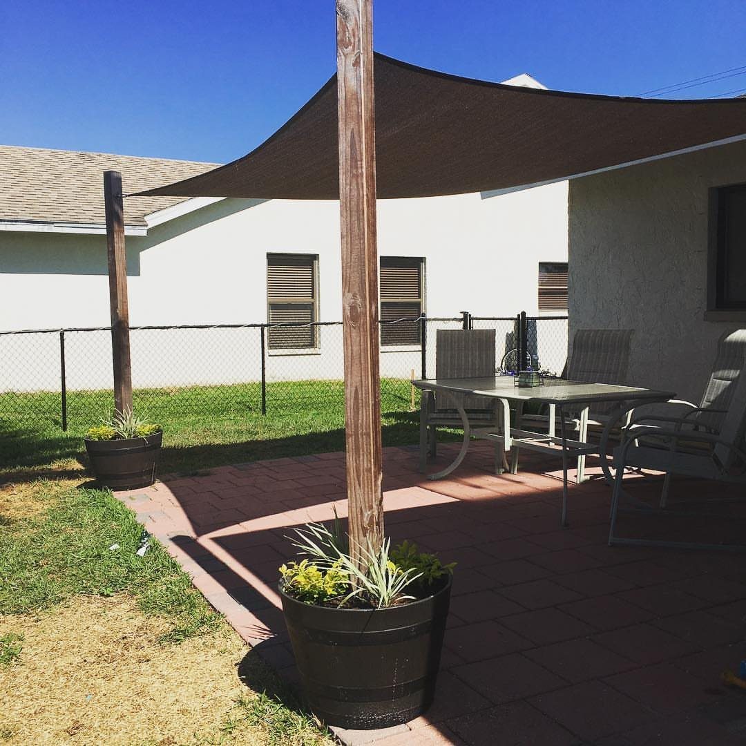 17 Deck Covering Ideas for Shade, Style & Rain Shelter 6 A dark brown triangular shade sail stretched over a patio with outdoor furniture.