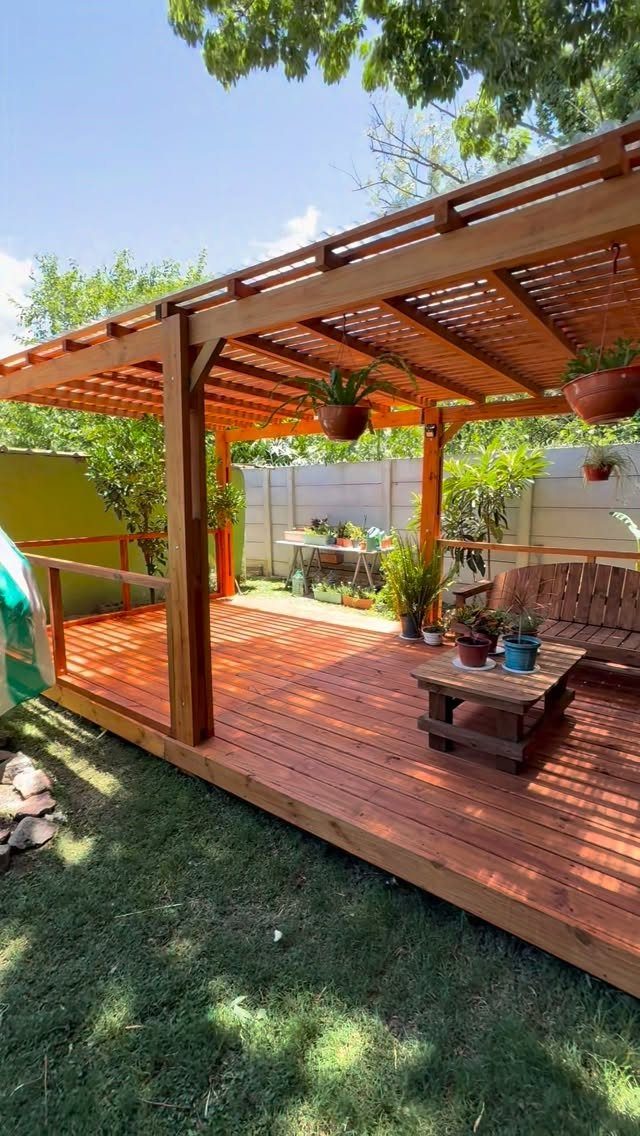 17 Deck Covering Ideas for Shade, Style & Rain Shelter 16 Wooden deck with a slatted pergola roof and hanging plants in a backyard setting.