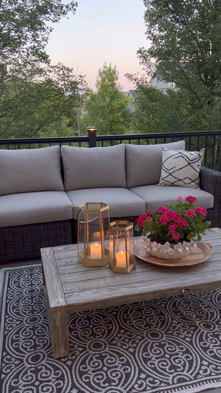 Deck on Front of House: 10 Ideas for Welcoming Style 1 Grey outdoor sofa and wooden coffee table with lit candles and pink flowers on a deck.