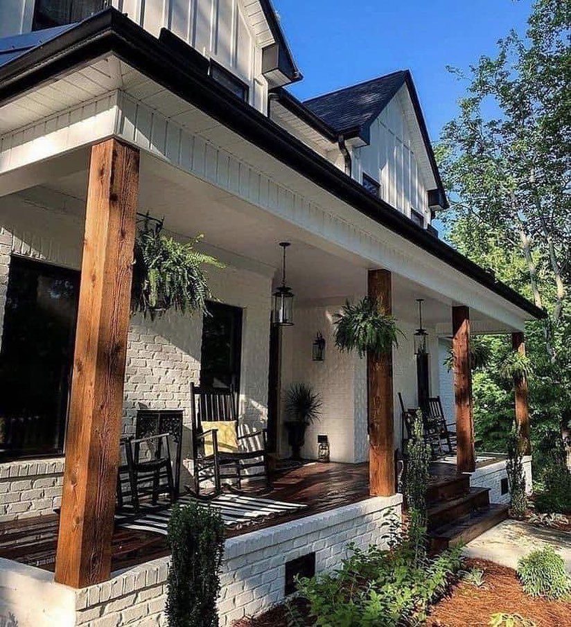 Deck on Front of House: 10 Ideas for Welcoming Style 7 White brick farmhouse porch featuring dark wood flooring, wooden pillars, black rocking chairs, and hanging ferns.