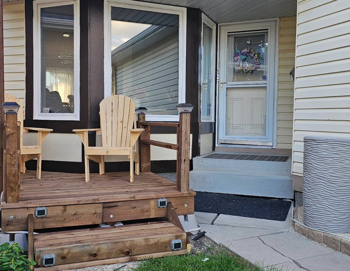 Deck on Front of House: 10 Ideas for Welcoming Style 10 Two wooden Adirondack chairs sit on a small wooden deck in front of a house.