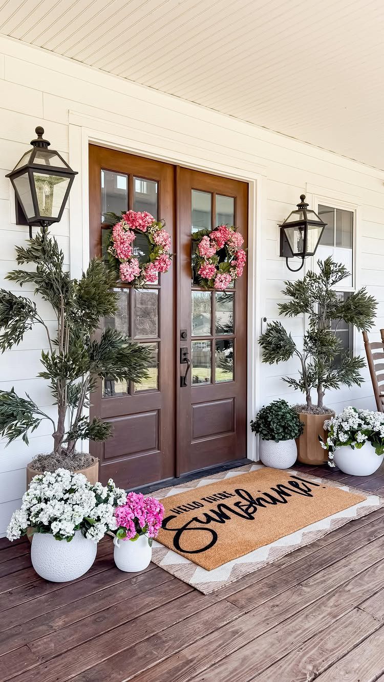 Deck on Front of House: 10 Ideas for Welcoming Style 3 Potted plants with white and pink flowers arranged on a wooden porch in front of brown doors.
