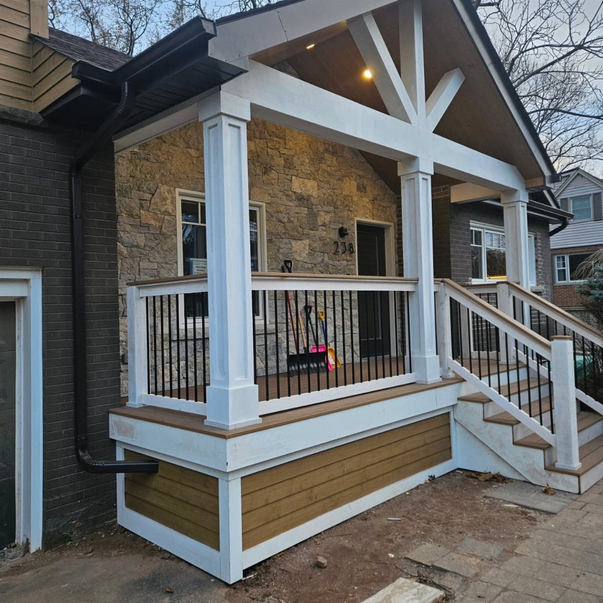 Deck on Front of House: 10 Ideas for Welcoming Style 6 A wide covered porch with white pillars, wooden beams, and a stone house facade.