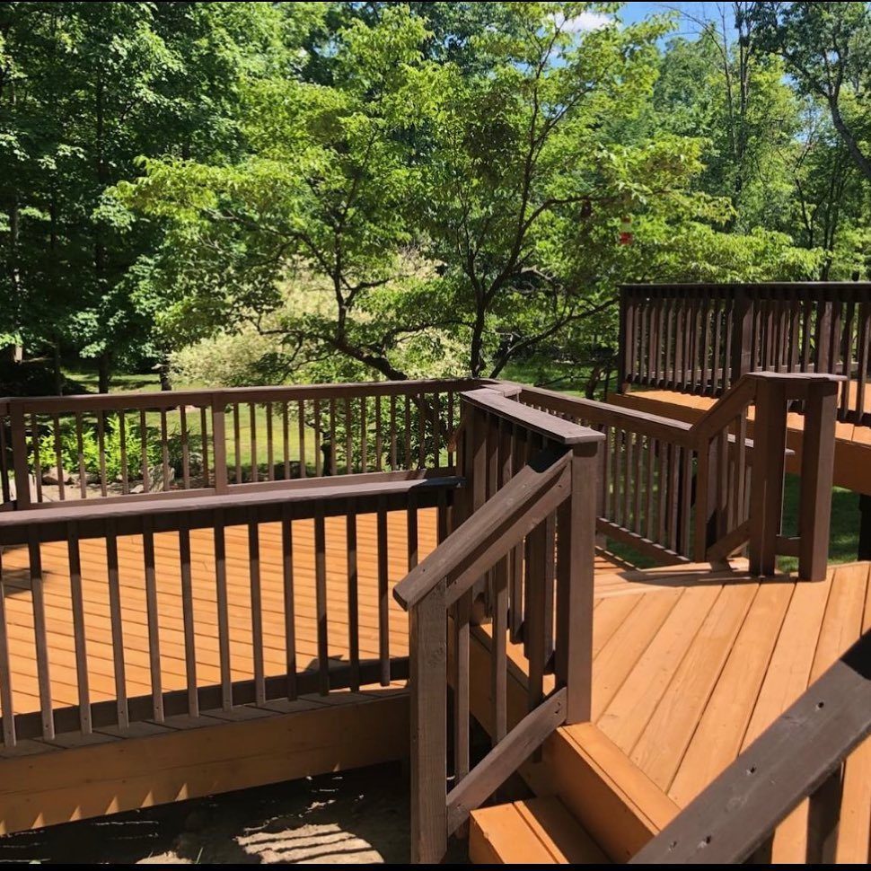 A multi-level wooden deck with brown stain and railings surrounded by green trees.