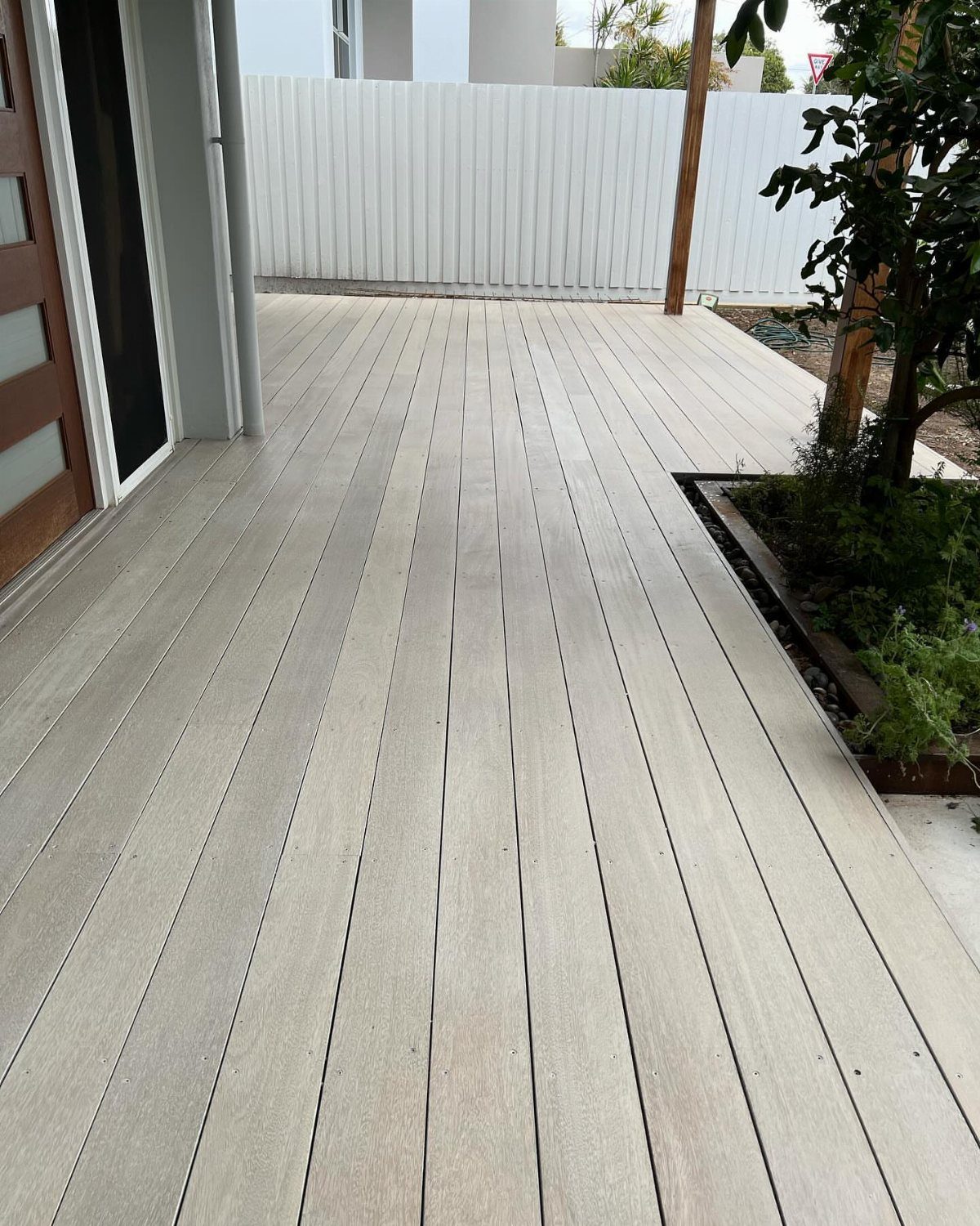 Light gray whitewashed wooden deck planks leading toward a white fence and garden.