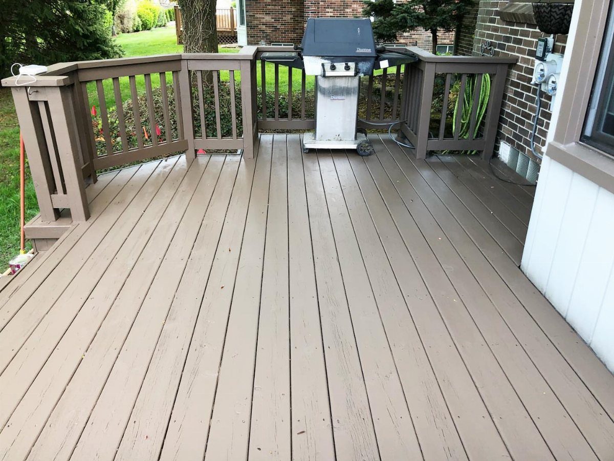 A large wooden deck stained in a light taupe color with a grill in the corner.