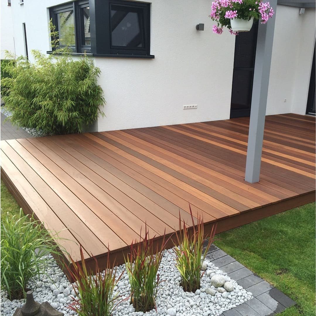 Wooden deck with planks in multiple shades of brown stain next to a white house.