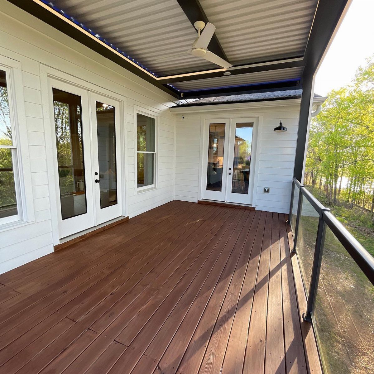 A wooden deck with a rich brown stain attached to a white house with glass doors.