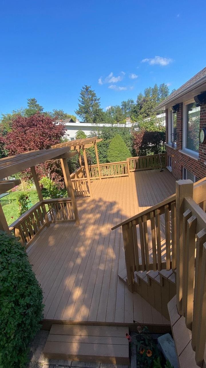 A large wooden deck with a pergola and railings stained in a warm cedar tone.