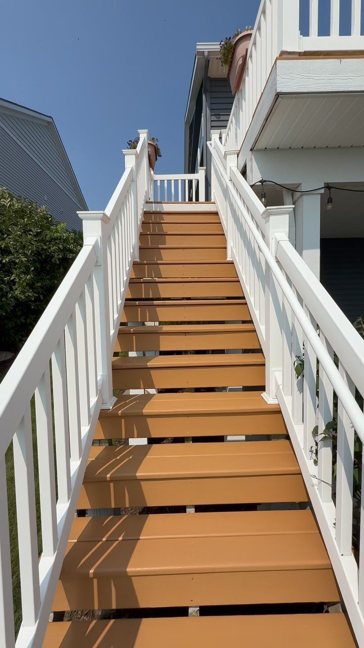 Tan painted wooden stairs with white railings leading up to a house under a blue sky.