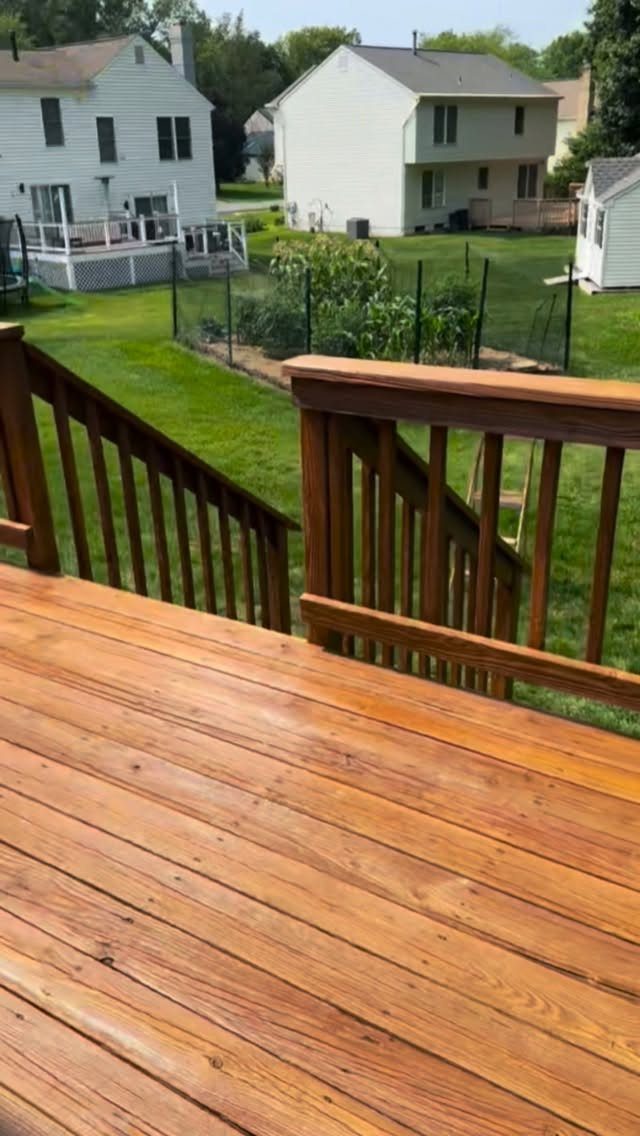 A wooden deck with a warm honey stain overlooking a green lawn and suburban houses.