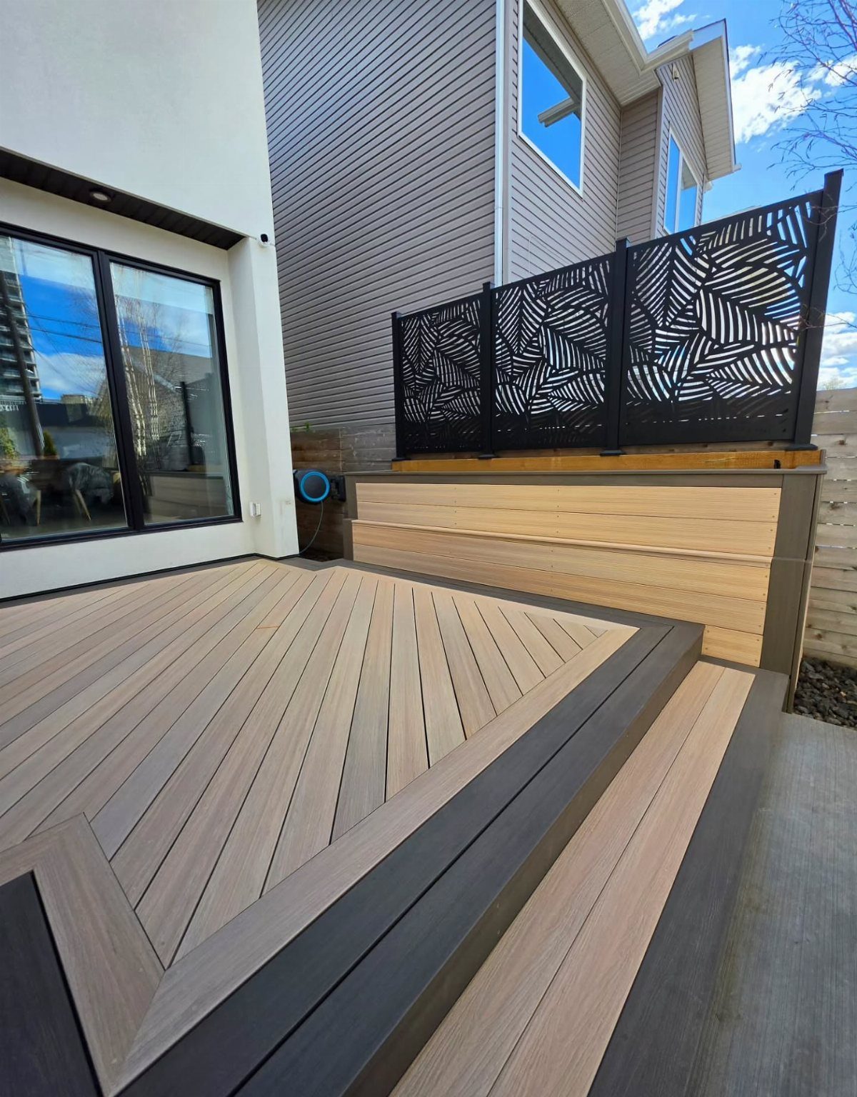 Modern wooden deck with geometric plank patterns and dark grey trim next to a house.