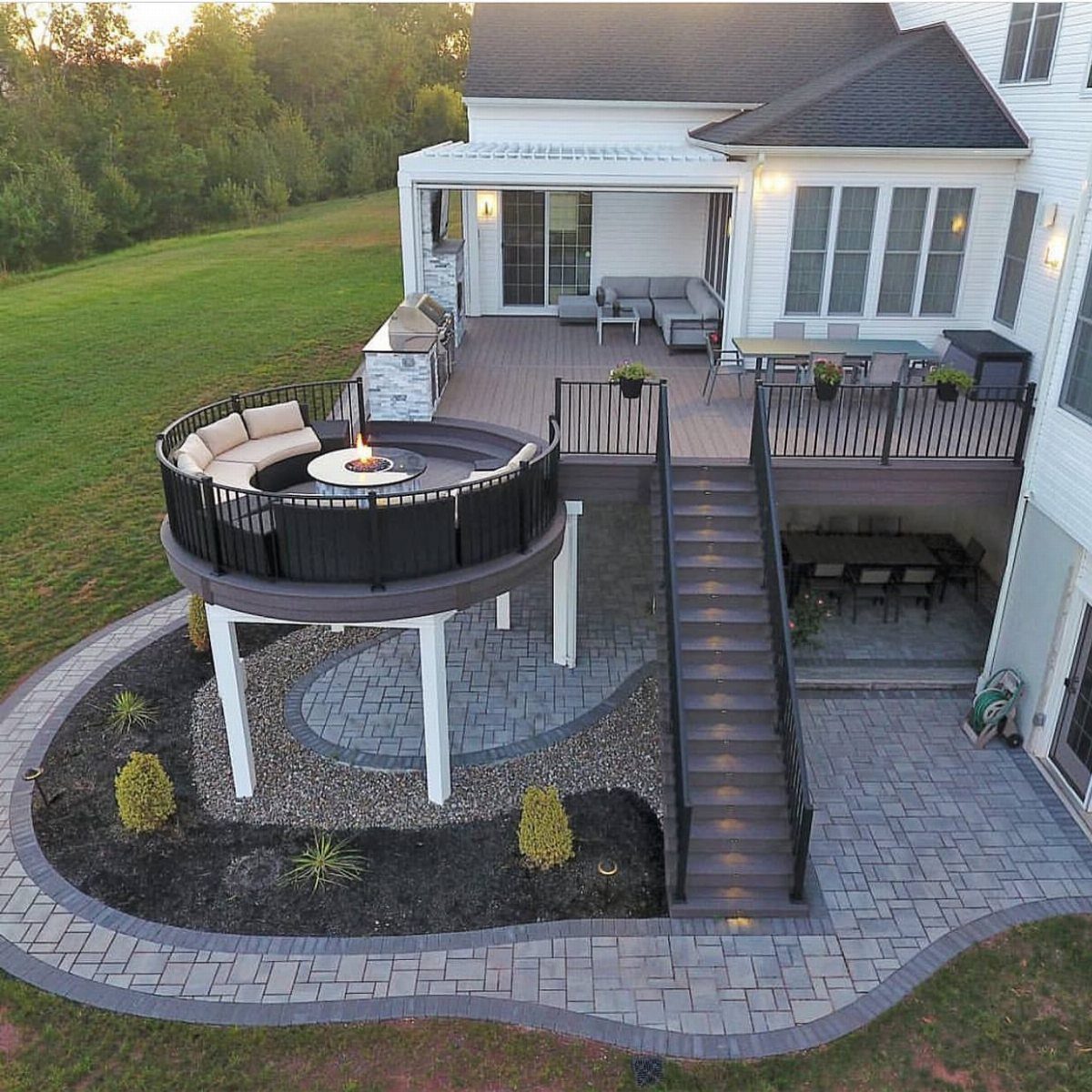 A multi-level outdoor living space featuring a circular deck, stairs, and a stone patio.