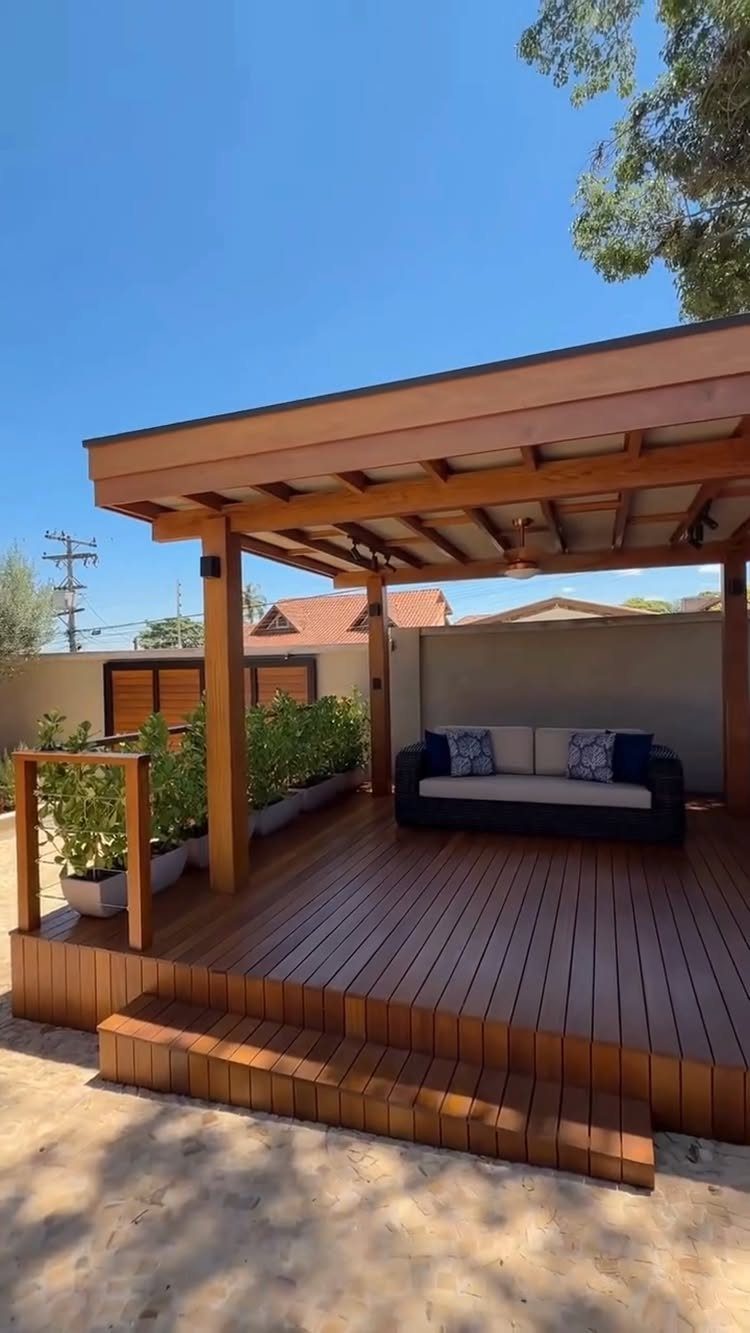 Wooden deck with a large pergola covering a modern outdoor sofa and potted plants.