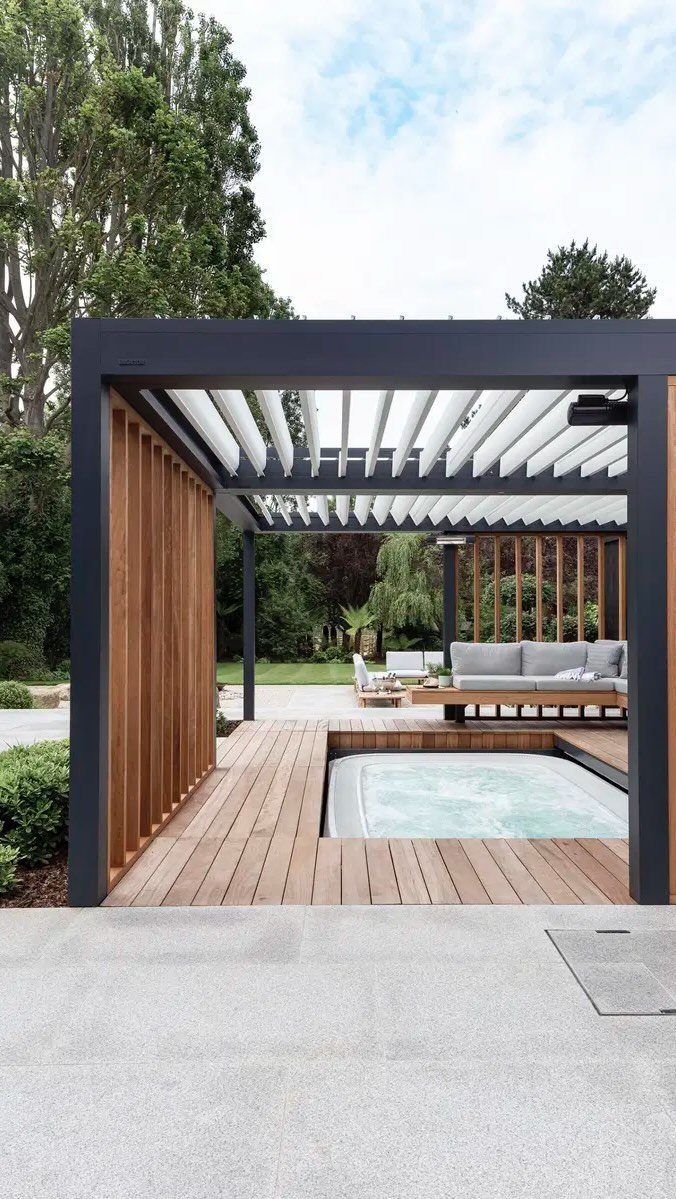 Wooden deck with an integrated hot tub meeting a light grey stone patio under a pergola.