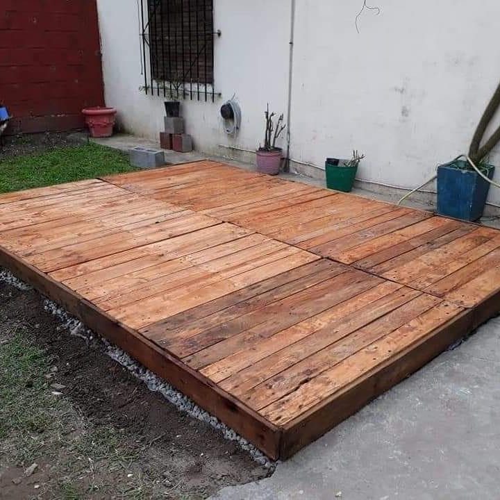 A low wooden deck constructed from rustic planks situated outdoors next to a white building wall.