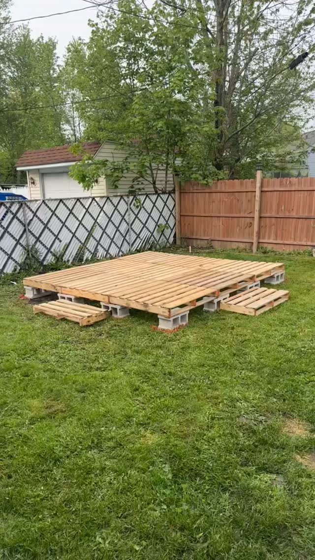 A pallet deck constructed on a lawn using white concrete blocks for support.