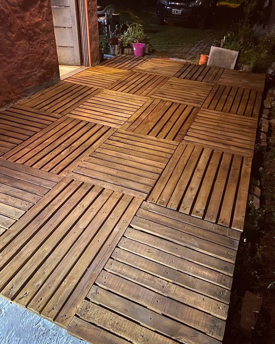 A wooden deck constructed from multiple stained pallets arranged in a grid pattern outdoors.