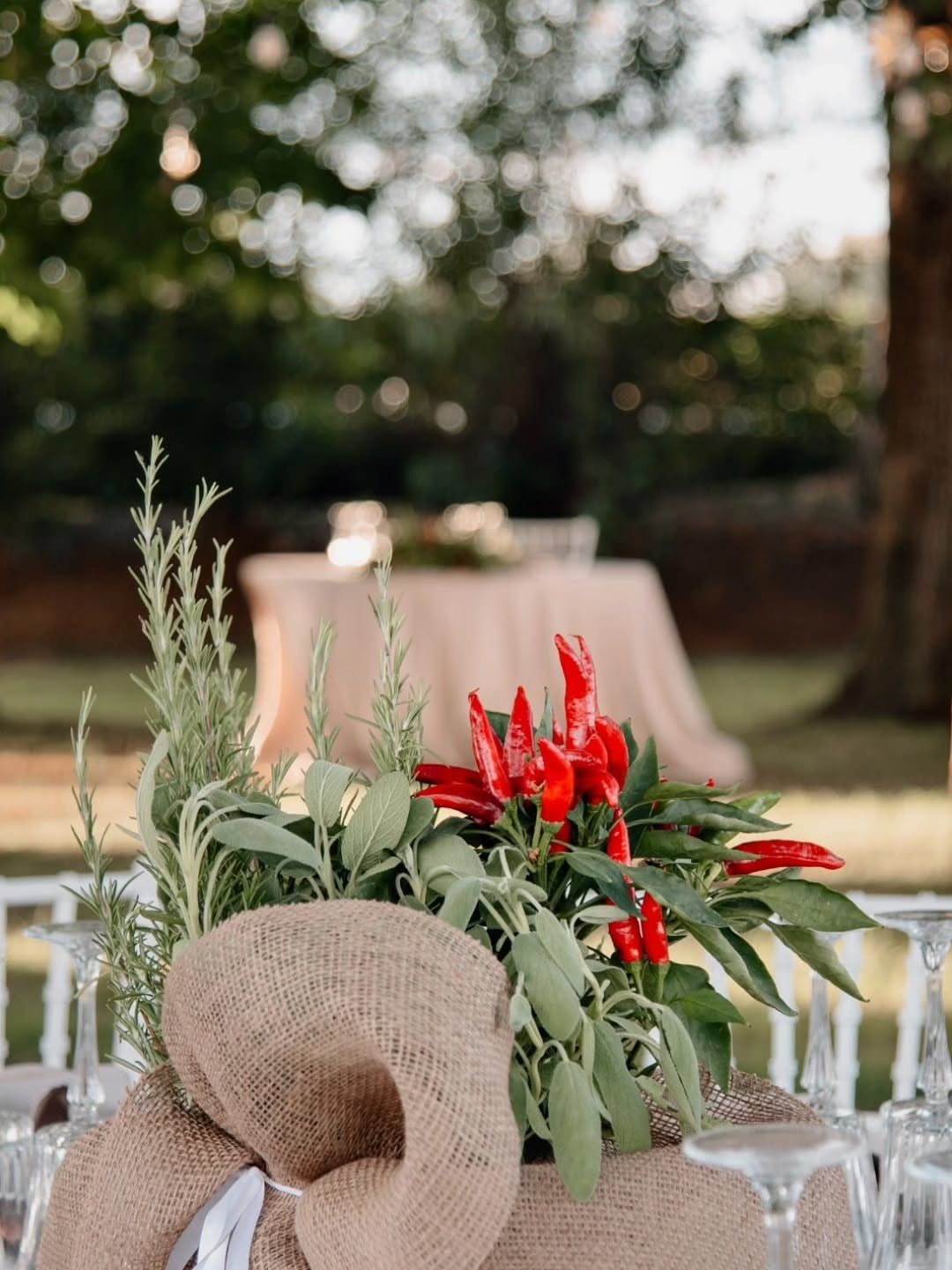 Green herbs and red chili peppers arranged inside a rustic burlap sack centerpiece on a table.