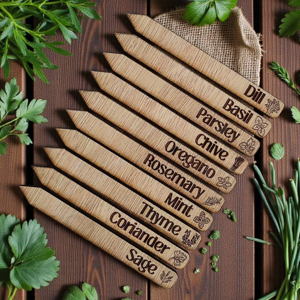 Engraved wooden herb garden labels arranged on a dark wooden surface with fresh green herbs.