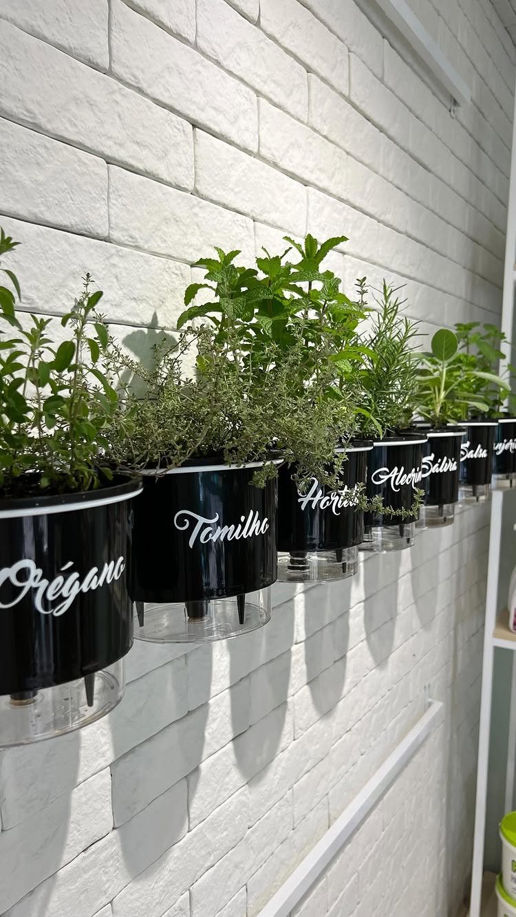 Black cylindrical herb planters with white labels mounted on a white brick wall.