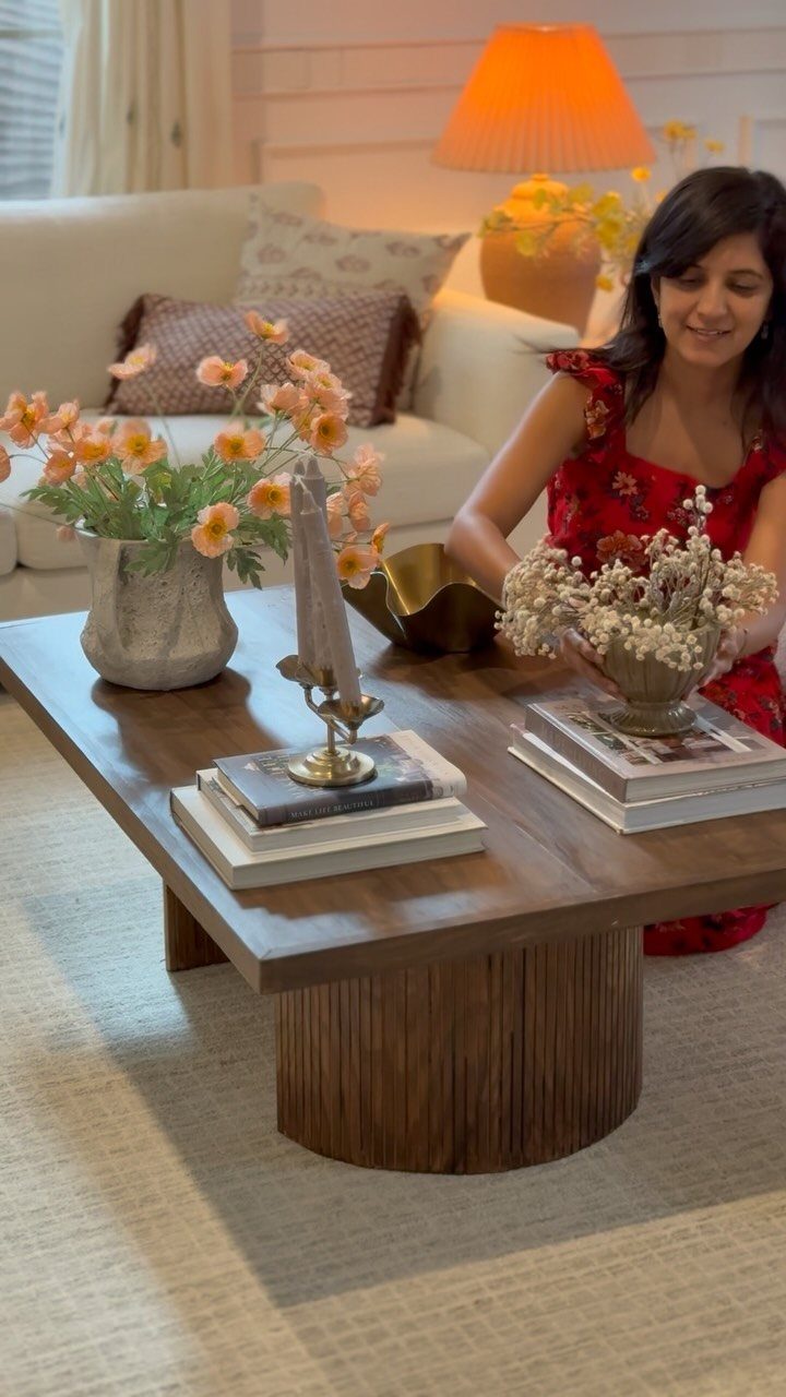 A woman arranging decorative items on a large wooden coffee table in a living room.