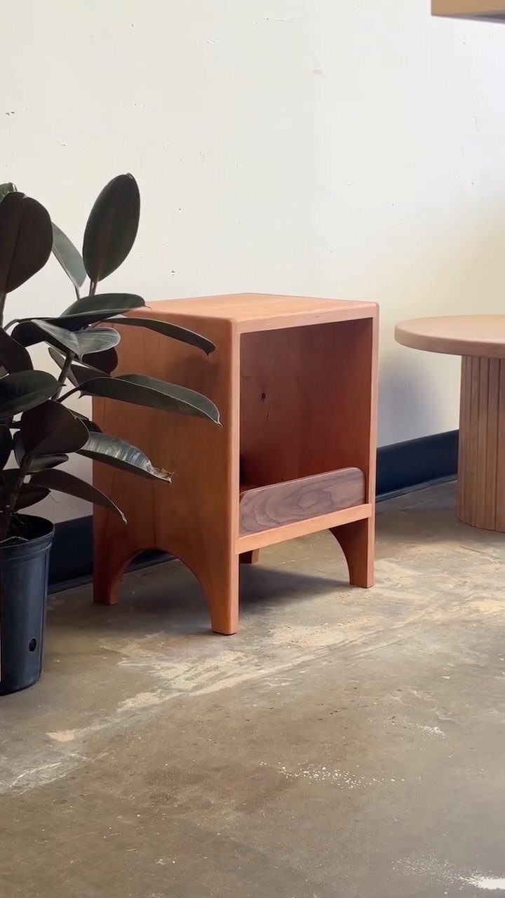 A small wooden side table with an open shelf and arched legs on a concrete floor.