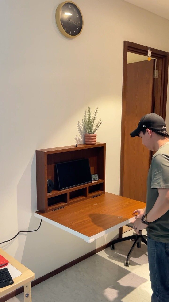 A wooden wall-mounted desk with a hutch stands against a white wall near a man.