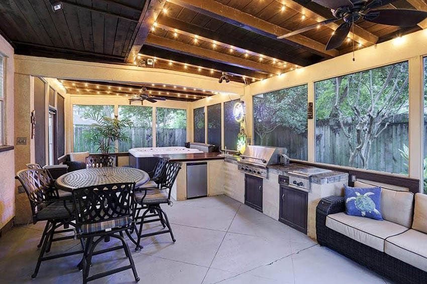Outdoor kitchen with grill and dining area located under a wooden deck ceiling.