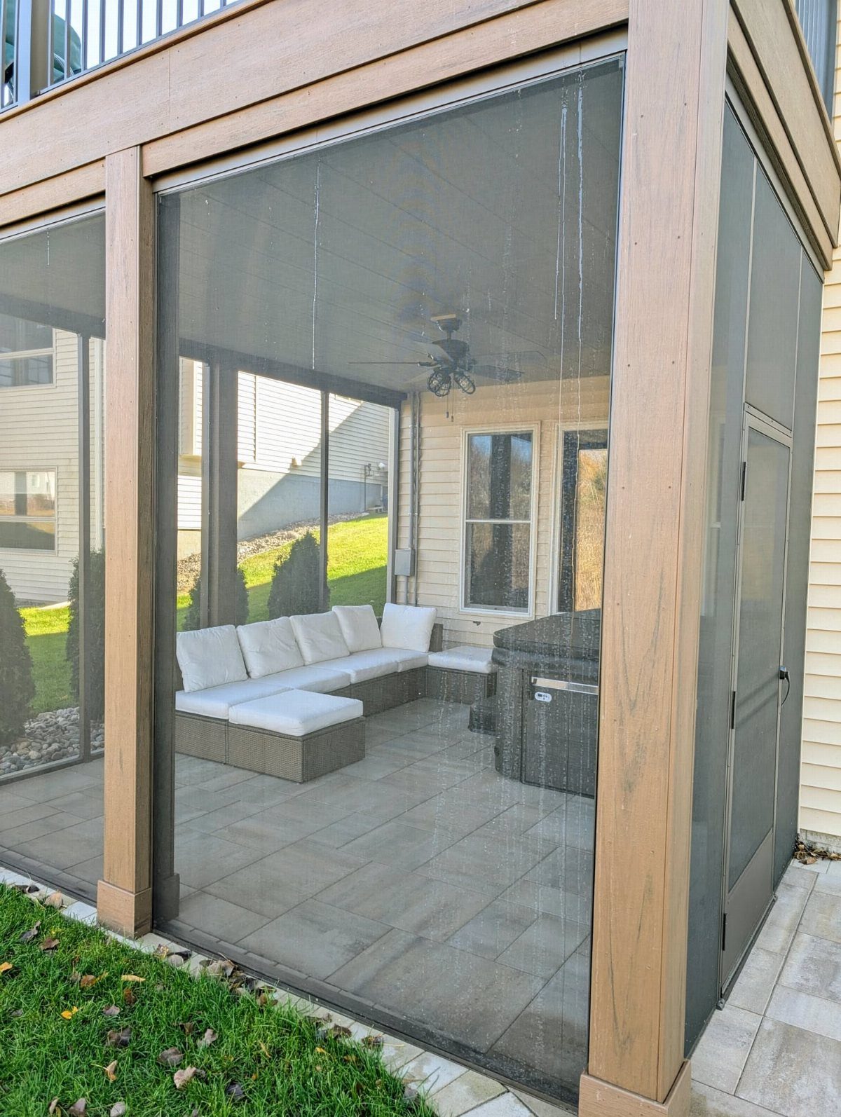 Screened-in porch under a deck with white sectional seating and a hot tub.