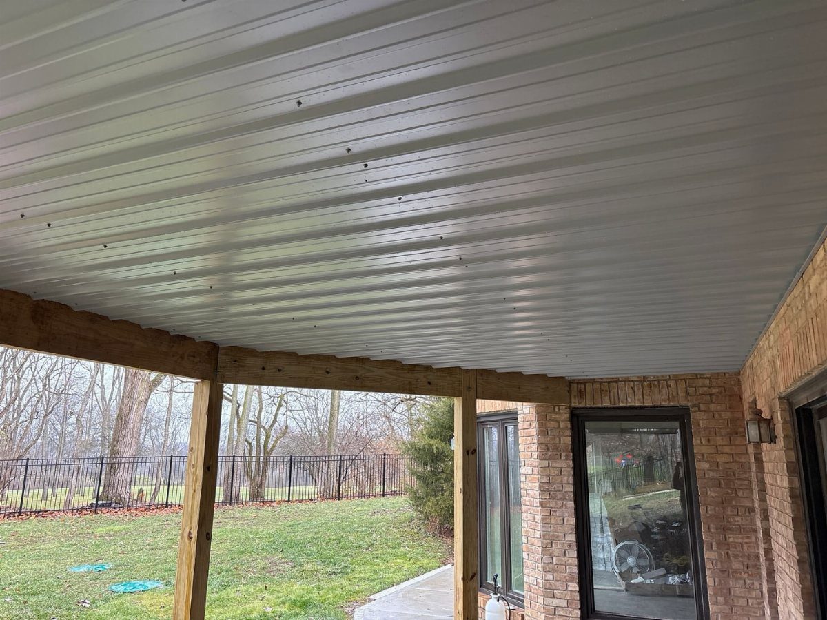 White corrugated under-deck roofing system installed beneath a wooden deck structure overlooking a yard.