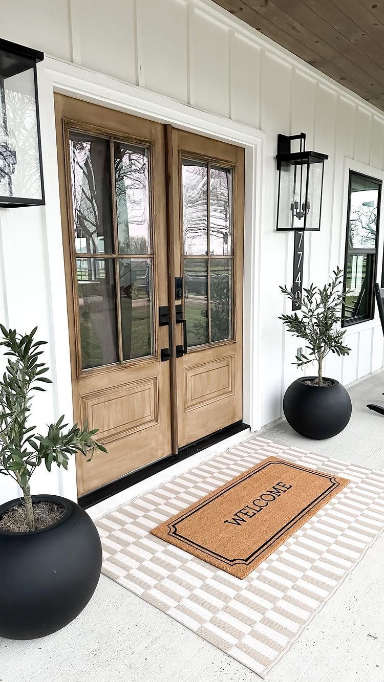 Wooden double doors with glass panes set against white board and batten siding on a porch.