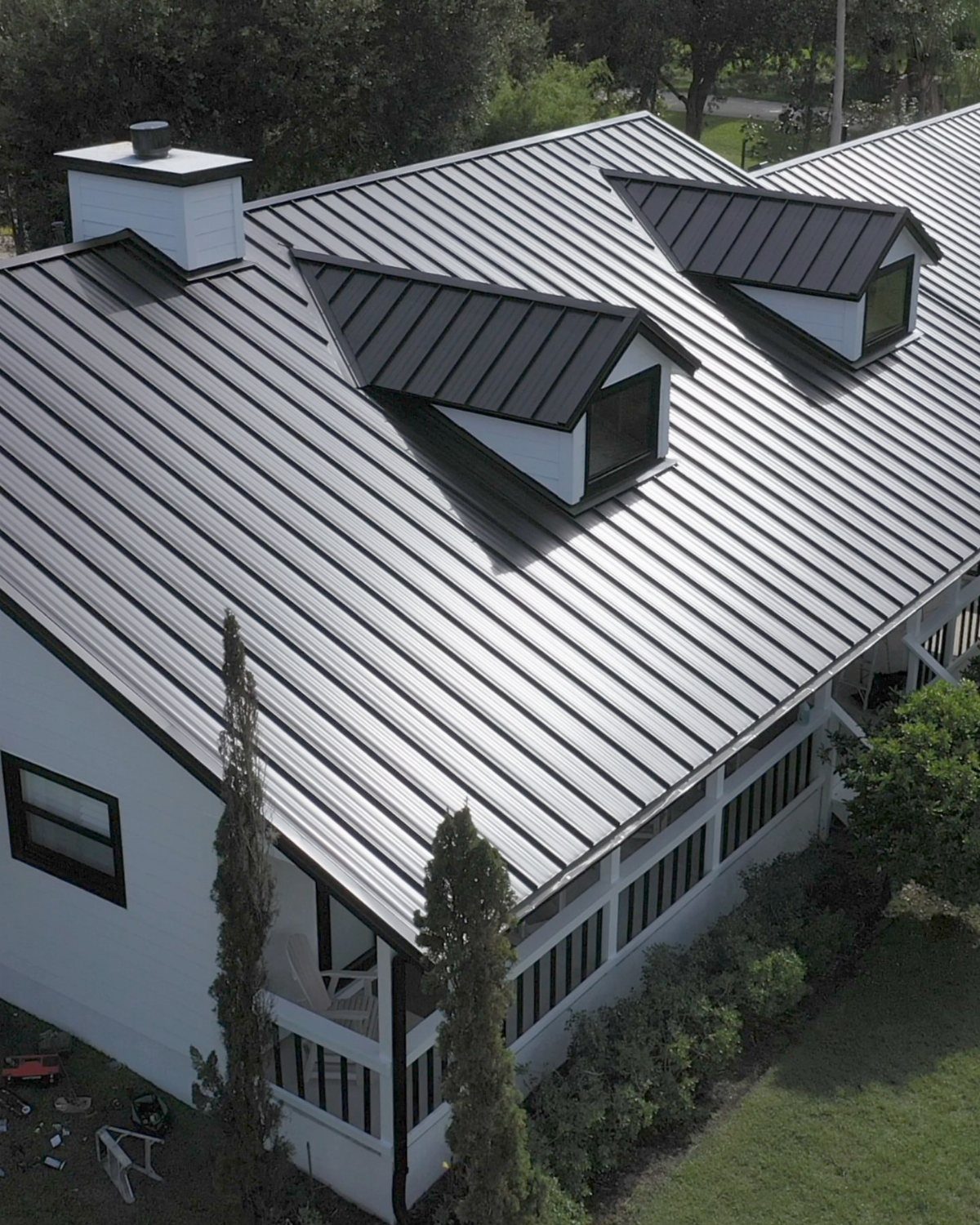 Dark grey standing seam metal roof on a white farmhouse with dormer windows.