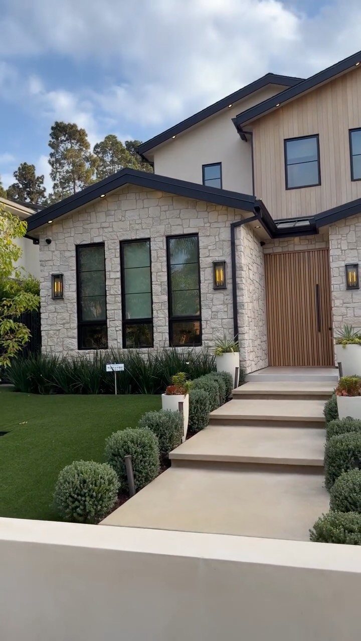 Modern house exterior featuring light stone walls, vertical wood siding, and large black-framed windows.